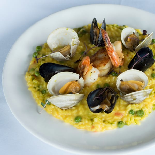 Seafood risotto with clams, mussels, shrimp, and scallops on a white plate.