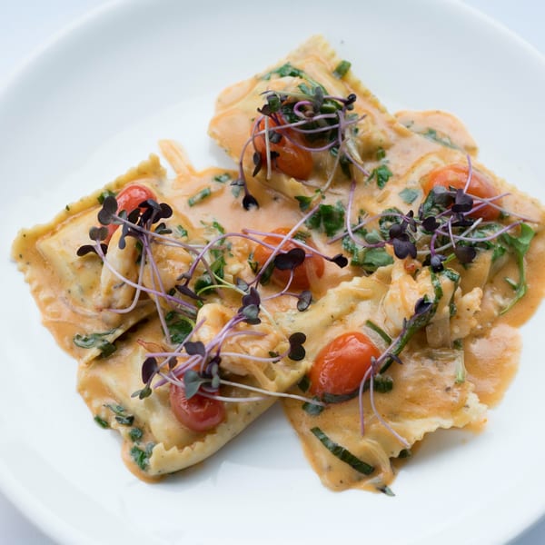 Dolce Restaurant's ravioli dish, garnished with cherry tomatoes, fresh herbs, and microgreens.