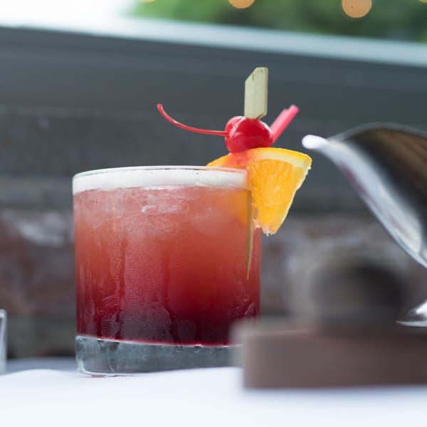 Red cocktail with an orange slice and cherry garnish, condensation on the glass.