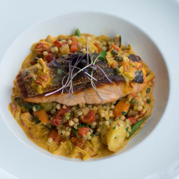 Pan-seared salmon with crispy skin, served over couscous, vegetables, and a creamy sauce.