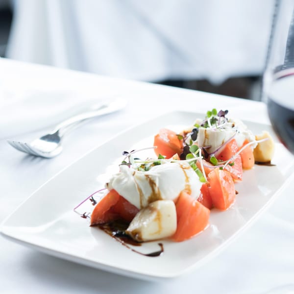 Caprese salad with fresh mozzarella, sliced tomatoes, balsamic glaze, and microgreens on a white plate.