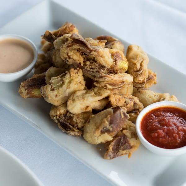 Crispy fried mushrooms with two dipping sauces, one red and one creamy, on a white rectangular plate.