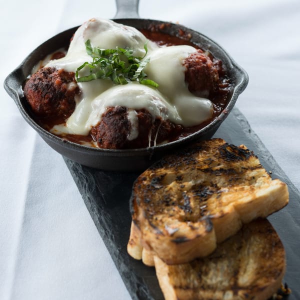 Italian meatballs with melted mozzarella and fresh basil in a cast iron skillet, served with grilled toast.