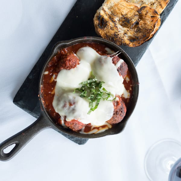 Italian meatballs in a cast iron skillet with melted mozzarella and basil, served with grilled bread.