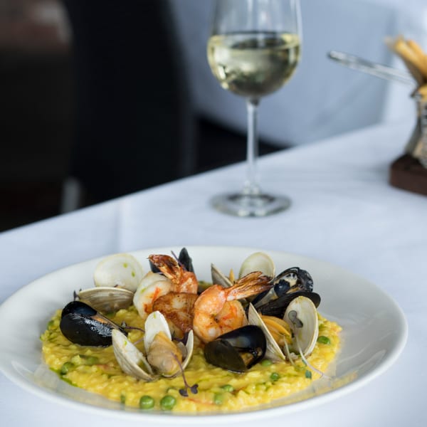 Seafood risotto with shrimp, mussels, and clams, alongside a glass of white wine.