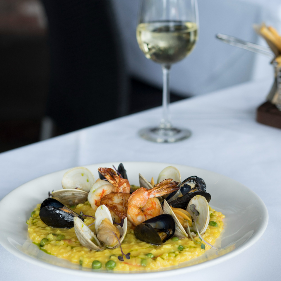 Seafood risotto with shrimp, mussels, and clams, alongside a glass of white wine.
