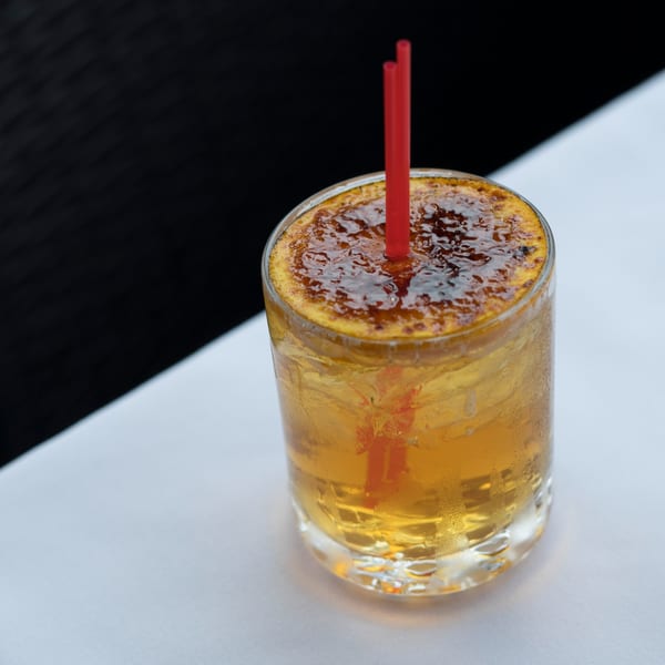 A Dolce Restaurant cocktail with a caramelized sugar top and red straws on a white tablecloth.