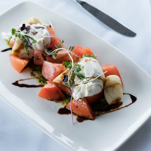 Caprese salad with fresh mozzarella, sliced tomatoes, basil, and balsamic glaze on a white plate.