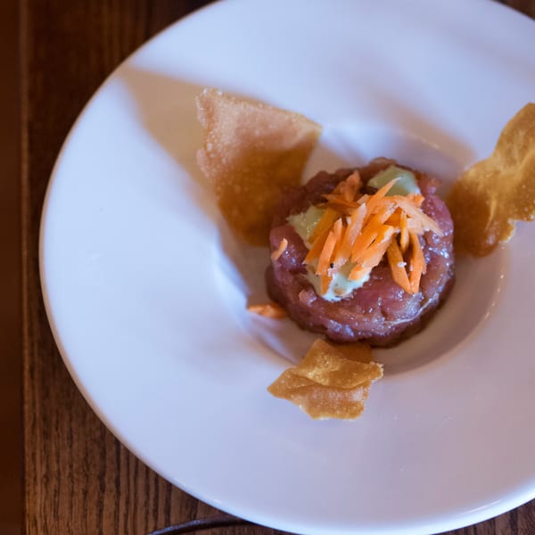 Tuna tartare topped with shredded carrots and a creamy sauce, served with crispy wonton chips.